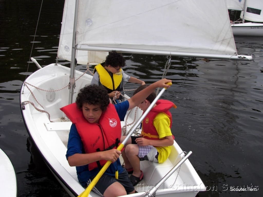 3 Scouts trying to paddle small sailboat out of crowded dock
