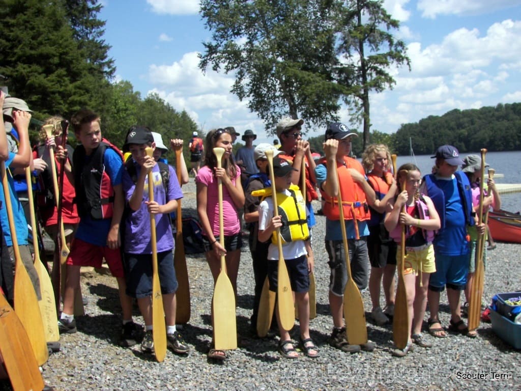 several Scouts holding their paddles, waiting for the safety talk before canoeing